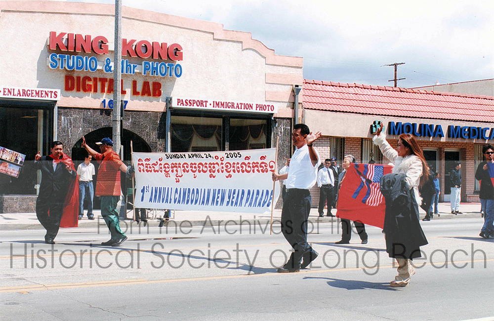 Men and women on Anaheim Street, Long Beach, CA. They are holding a banner which reads: Sunday April 24, 2005, 1st Annual Cambodian New Year Parade.