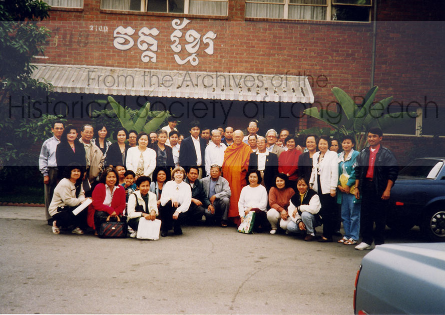 Students and teachers from an English language class stand in front of the Wat Khemara Buddhikaram (Khmer Buddhist Temple) where social programs and English classes were provided throughout the 1990s. The temple, headed by Ven. Kong Chhean (in orange robe), moved to its current location in the former Oil, Chemical, and Atomic Workers International Union Hall at 2100 Willow Street in 1988. The Khmer lettering on the building translates to Wat Khmer. Community members refer to the temple as Wat Willow after the street it is on.