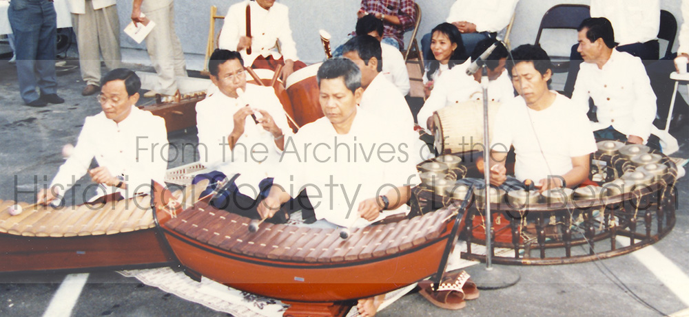 In this photo, Pon Yinn (second row, left) plays the flute while directing pin peat musicians at a community event performance.
