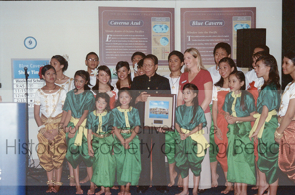 On Southeast Asia Day in October 2008, the Long Beach Aquarium of the Pacific honored Pich Yon with its Heritage Award for his contributions to the Cambodian community. The award recognized him as a steward of Cambodian culture through preserving Cambodian art as well as through his service to the community. Pich Yon is one of the founders of the Cambodian Association of America (CAA) and has served on its board for more than 30 years. In this photo, he is surrounded by the youth performers as he receives the award.