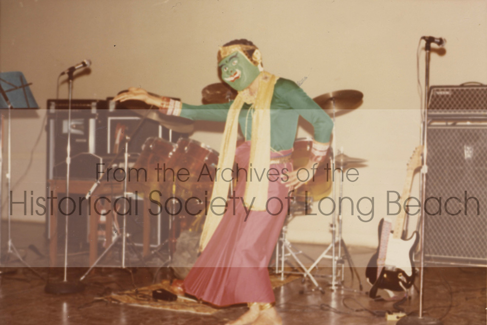 Pich Yon performs comedic dance in between music sets for a Cambodian band (circa 1977). He wears a green mask with a green blouse and red sarong.