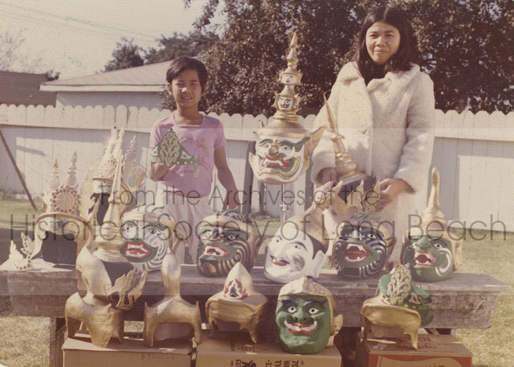 This photo showcases a collection of masks created by Pich Yon in the early 1980s for Cambodian performances. In the image, Pich Yon's wife and son are seen holding examples of mask components.