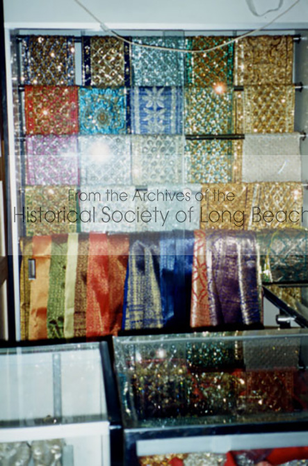 Hand beaded and sequined sashes and hand woven silk fabric hang in a display case in Banteay Srey, a clothing store and wedding planner in Long Beach, CA.