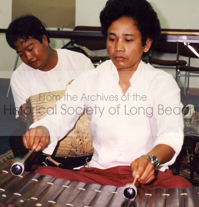 Close-up Image of musician playing the Roneat Ek. The Roneat Ek is a type of xylophone that is played in Pin Peat and Mohori ensembles. The Roneat Ek consists of a series of wooden bars, each of varying lengths, arranged in a wooden frame. The musician uses mallets to create distinctive ringing tones.