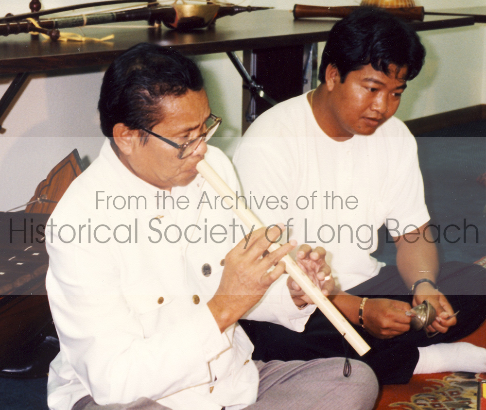 Close-up image of Master Yinn Ponn playing the flute. Young student plays the small hand cymbals.