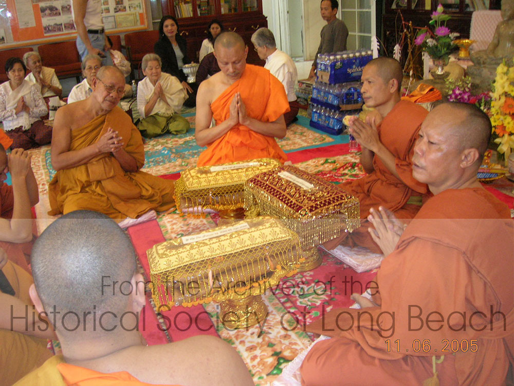 During the rainy season in Cambodia, which last about three months, monks remain in the temple. At the end of the rains, lay people present the monks with new robes during a ceremony called Bun Kathin. The robes have been placed on trays and covered with a “tray” (pronounced trai). Pictured here are monks chanting over the new robes.