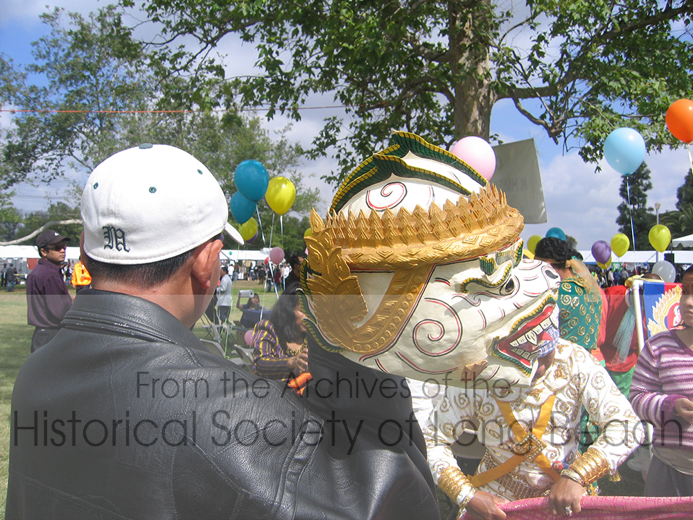 Cambodian New Year celebrations in Long Beach include performances of traditional dance and music. This photo is a close up of a Hanuman mask. The performer that wears the mask is behind it dressed in white and gold. Hanuman is the Monkey King of the epic poem, Ramayana (known as Riemke in Khmer). The story tells of the banishment, travels, and return of Prince Rama and his wife Sida. Originating in India, the Ramayana is now found throughout Southeast Asia.