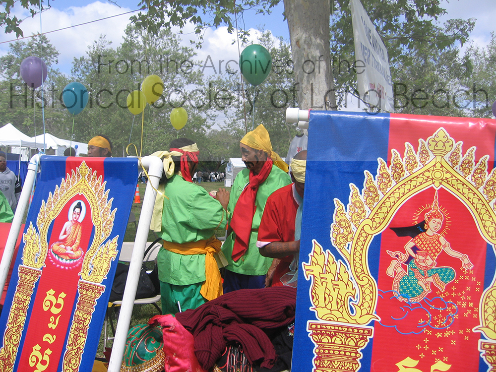 Two men prepare to perform Chhayam, a lively call and response dance performance using primarily percussion instruments. The banner on the left has an image of the Buddha and reads Sua Sdey Chnam Tmey (Entering the New Year). The banner to the right shows the New Year Angel. Each year a new angel arrives to protect and bring blessings to the people.