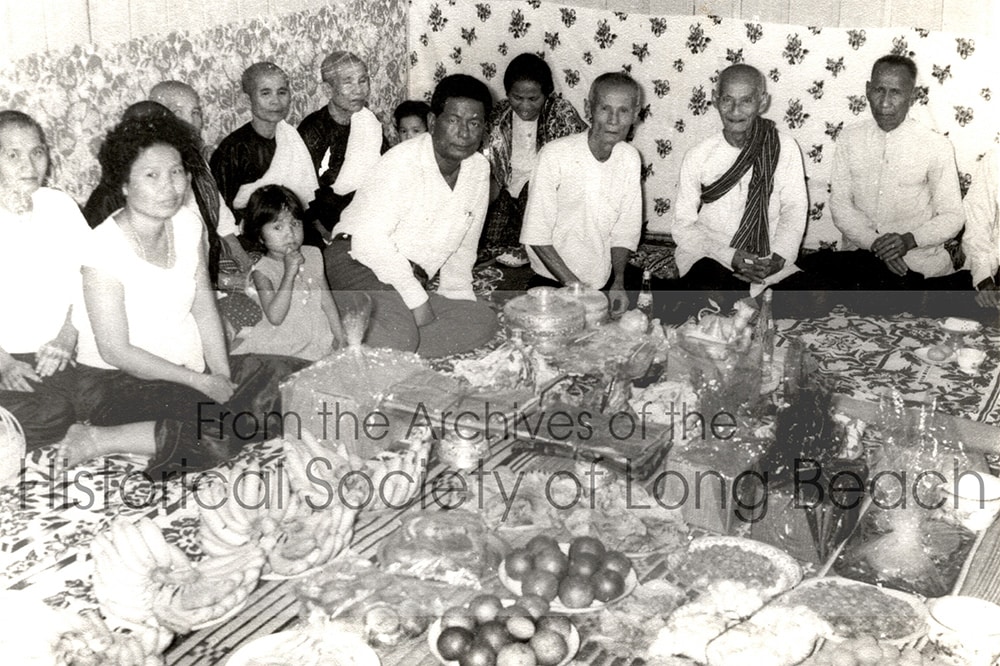Bokanika Kan’s maternal grandmother, Sieng Torng (front row, far left), and maternal grandfather, Chhung Pen (front row, 3rd from left) with guests and family. Food offerings suggest it could be a wedding c. 1960.