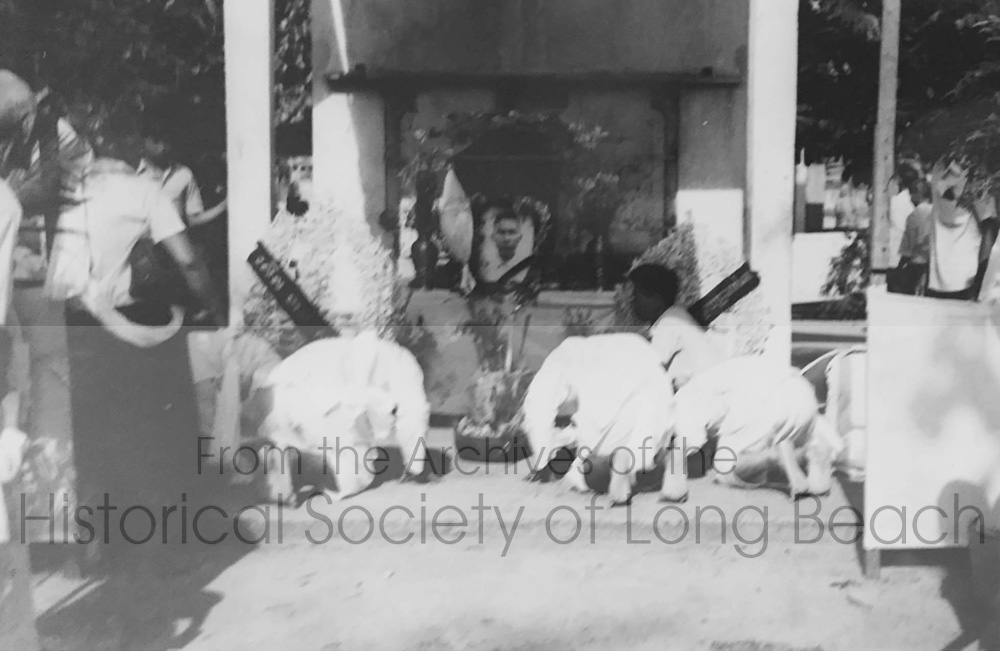 Funeral of Clark Tang’s grandfather, Cheark Ung, at a temple in Phnom Penh, Cambodia 1974. Clark’s family is Chinese and some traditional aspects of a Chinese funeral can be seen. The presence of the coffin and photo means the body has not yet been cremated. Family members bow to show their respect and say goodbye.