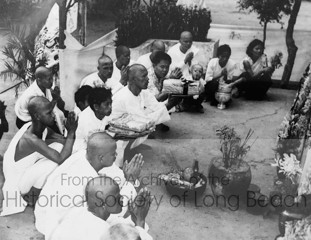 Funeral of Clark Tang’s grandfather, Cheark Ung, at a temple in Phnom Penh, Cambodia 1974. Clark’s family is Chinese and some of the traditional aspects of a Chinese funeral can be seen. Family members chant as part of the final goodbye and offer gifts to the deceased. Blood relatives of the deceased shave their heads. Those with hair may be friends or relations but not blood related.