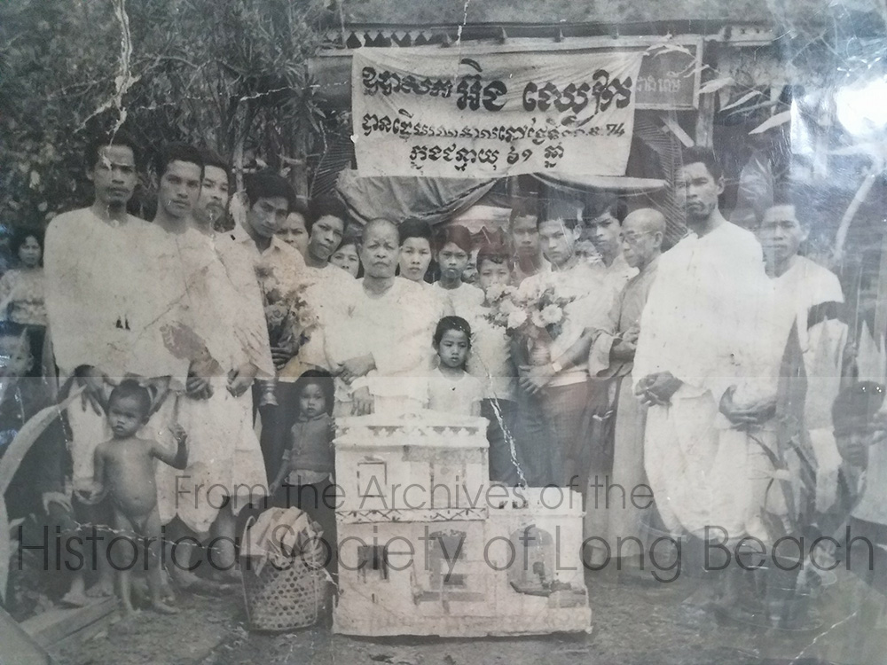 Clark Tang’s family in late 1974 or early 1975, at a 100 day memorial service in Svay Sisophon for his maternal grandfather, Cheark Ung. Clark’s uncles prepared the paper house at the center of the photo as well as special food and paper money which were all burned as offerings to the deceased and to ensure the well-being of the family’s ancestors.