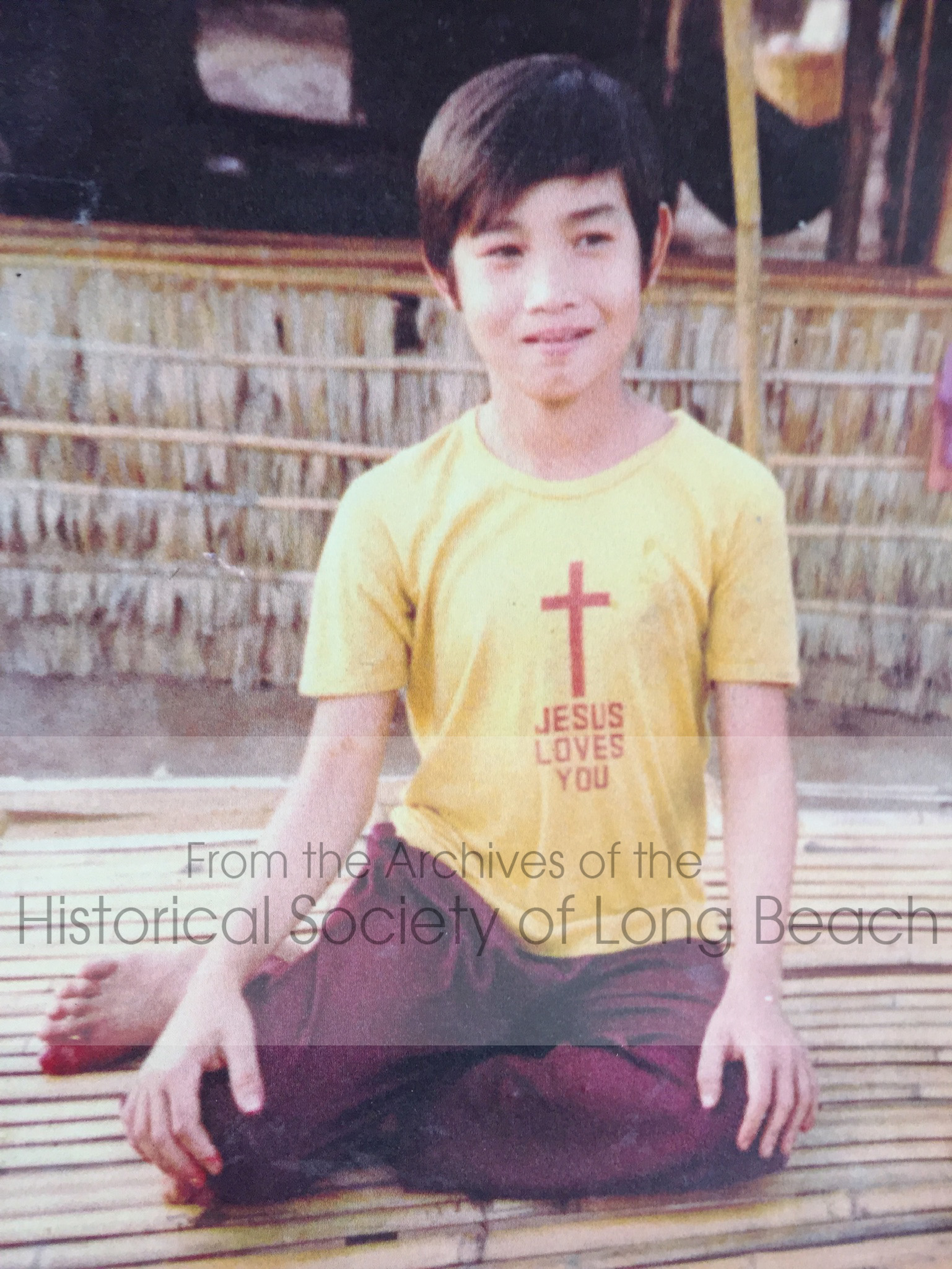 Clark Tang at the Khao-I-Dang refugee camp in Thailand, c. 1980. His t-shirt was provided by one of the Christian missions at the camp. Cambodians escaped the country with only the one set of clothes they had worn during the previous four years, so new clothing was highly valued. It was at this time that Clark started to know and accept God, 1980.