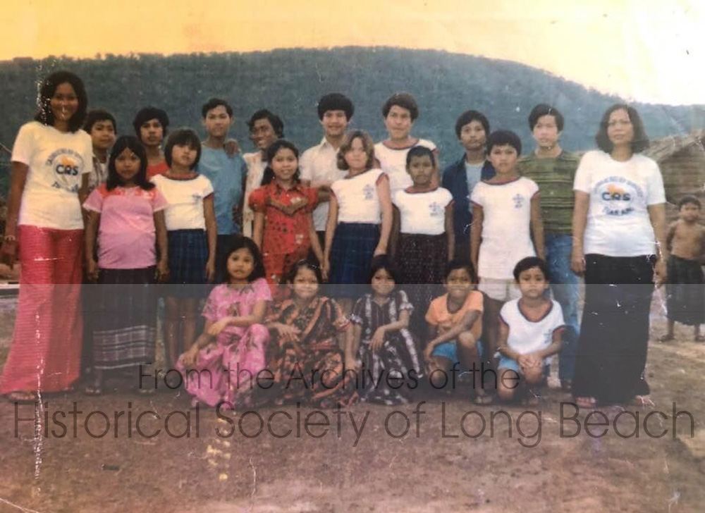 Janet Vanniroth with children at the orphanage at Khao-I-Dang refugee camp, Thailand, 1980. Janet is in the second row, wearing a red dress. Her mother, Vannsath Nguon, is at the far right wearing a white CRS (Catholic Relief Services) t-shirt with black pants. CRS may have been overseeing the orphanage operations. The woman at the far left, also wearing the CRS t-shirt, worked at the orphanage. Janet identified her as Auntie Ray. She is not a blood relative, but it is a common practice in Cambodia to address everyone using kinship terms. The rest of the children are unidentified. Janet stayed in touch with Auntie Ray and visited her in Canada where she received sponsorship.