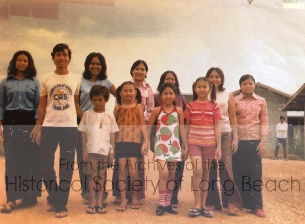 Janet Vanniroth with children and staff at the orphanage at Khao-I-Dang refugee camp, Thailand, 1980. In the back row, from left is one of the orphanage staff “mothers” (unidentified) and her husband (unidentified); next is Auntie Ray (She is not a blood relative, but it is a common practice in Cambodia to address everyone using kinship terms); other orphanage staff are unidentified. Janet is in the front row, 2nd from right, wearing a dress. The rest of the children are unidentified. Janet’s mother worked at the orphanage for nearly a year (1979 to 1980).