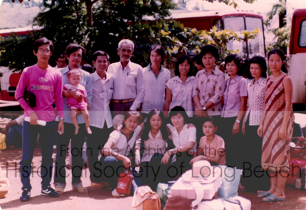 Kam Lou Lopez (front row, 2nd from left with long hair) with her family waiting to leave for the processing center in the Philippines before heading to the U.S., 1982. Their friends from Khao-I-Dang refugee camp came to say good-bye. Back row: Kam’s father, Man Lou (3rd from left) and her mother, Frang Phar, is third from the right. Other people unidentified.