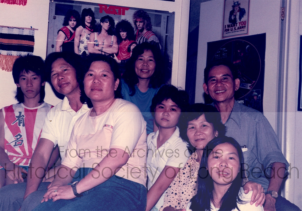 Kam Lou Lopez’s family in their two bedroom apartment in Marlborough, TN 1984. From left to right: Kam’s cousin, Avery; her uncle, Sy, who sponsored them; her mother, Fang Phar; Uncle Sy’s wife (in back wearing blue blouse), Aung Lucy; Kam’s sister, Meicy Lou; her father (in blue shirt) Man Lou; and cousin (in front far right) Seav.