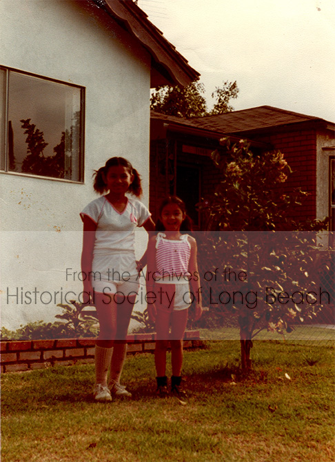 Monorom Neth’s sister, Somealy and their cousin, Sokunsothea Ouch, outside the house the two families (16 people altogether) lived when they first arrived in Norwalk, CA, 1983. Within the year, they moved to a smaller house.
