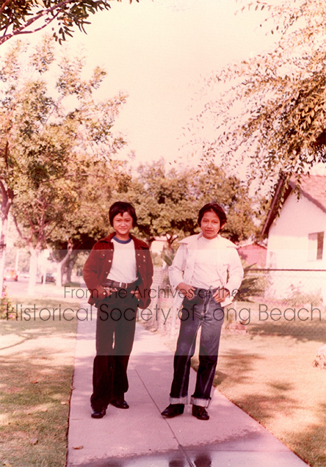 Monorom Neth (right) with his cousin, Someth Ouch, outside the house where the two families (16 people altogether) lived when they first arrived in Norwalk, CA, 1983. They may have lived there less than a year before moving to a smaller house.