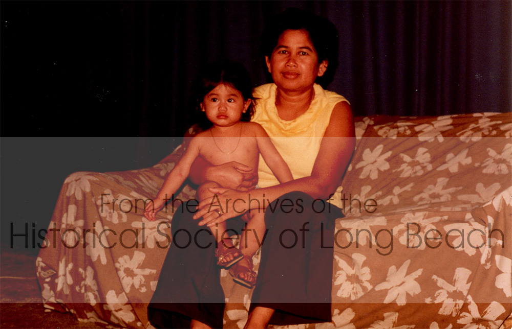 Monorom Neth’s mother, Om Van, with her niece, Christina Neth, Paramount, CA 1983. The two families (16 people altogether) lived in the house. The curtain behind the couch separated the living room into two rooms.