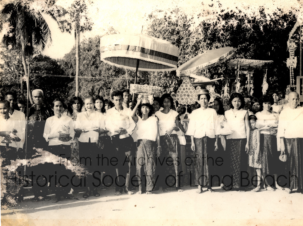 Namoch’s family and supporters gather for a temple fundraising procession at Kompong Cham market, Kompong Cham Hanchey, Cambodia, 1963. Second from right is Namoch’s maternal grandfather; paternal grandfather (white hair and black shirt); unnamed; grand aunt, Mu Noy; Namoch’s father, Luy Sokhom; Namoch’s mother, Thach In (holding an offering of new robes for the monks on her head); Luy Sokhom’s cousin, So An; Namoch’s maternal grandmother; and Namoch’s maternal aunt.