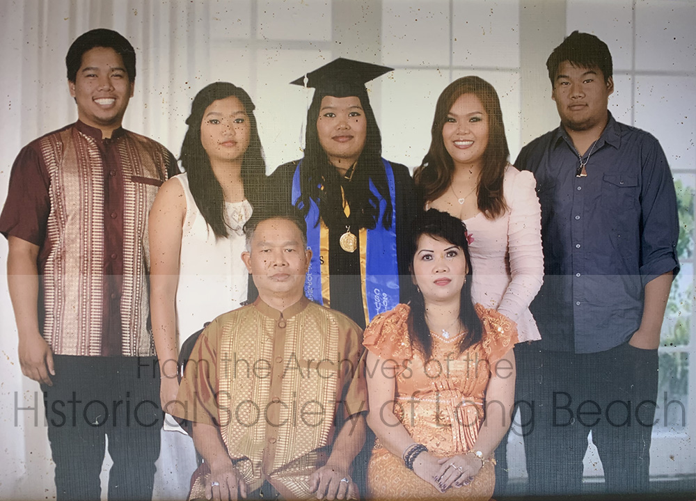 Rom Hoy and her family celebrating her daughter’s graduation from California State University, Long Beach in their home, Long Beach, CA, 2014. Back row from left to right: Rom’s son, Harrison Hoy; daughter, Annie Hoy; daughter, Terrie Hoy (in cap and gown); daughter, Chheng Jouy Hoy; and son, Havin Hoy. Front row, Lt to Rt: Rom’s husband, Chann Sao, and Rom (37 years old).