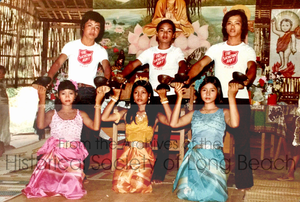 Sithy Yi (center) is performing the Coconut folk dance with her sister, Sithea (right), and a friend, Ouch (nickname), in a Buddhist temple in the Bataan Refugee Processing Center in the Philippines. The young man on the left in the back row is Rithear Chhang; the other two are unidentified. Each dance style has its own costuming convention, but the correct materials were not available in the camps, so performers improvised. Here the young women are wearing sarongs. The young men are wearing Salvation Army t-shirts and black pants in an attempt to be dressed alike.