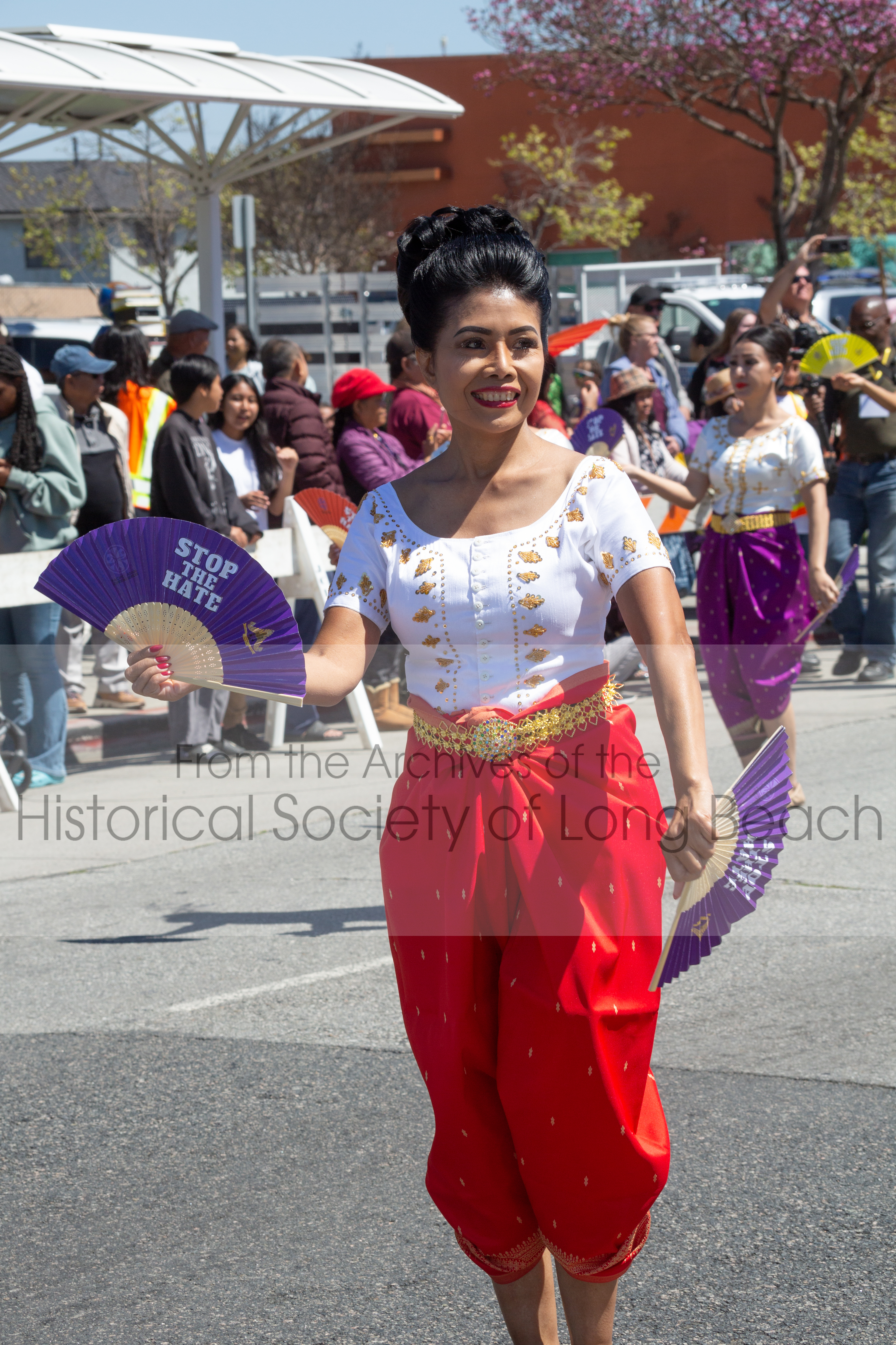 Sithy Yi leading the Stop the Hate with Love dance troupe marching on Anaheim Street, Long Beach, in the 2023 Cambodia Town Parade, April 2. The troupe carried banners and fans with the Stop the Hate message which was the parade theme that year. Sithy Yi has a strong commitment to the Cambodian community and participates in this event nearly every year in some capacity.