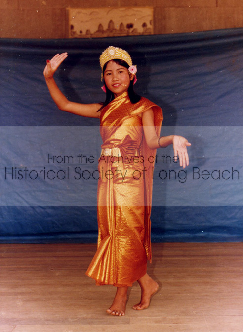Young woman dressed in Cambodian dance attire, poses on a stage in front of a blue screen.